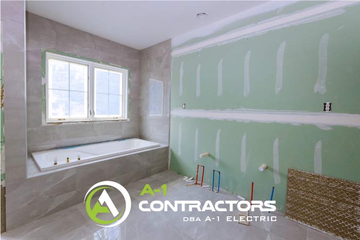Bathroom mid-remodel, showing new gray tile surrounding a soaking tub and green moisture-resistant drywall ready for paint, illustrating the construction phase of a major renovation.