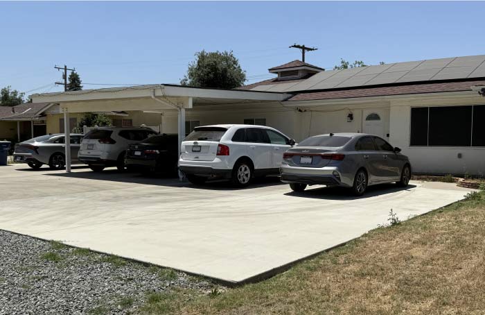 Completed concrete driveway and carport in front of a residential house with a solar panel installation on the roof, demonstrating exterior renovation services