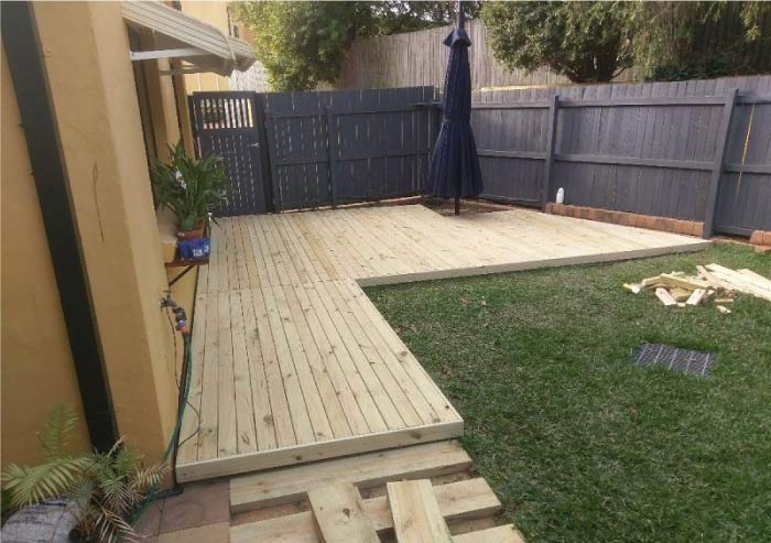 View of a newly constructed wooden deck and patio area in a backyard, ready for use, illustrating a completed exterior hardscape renovation project