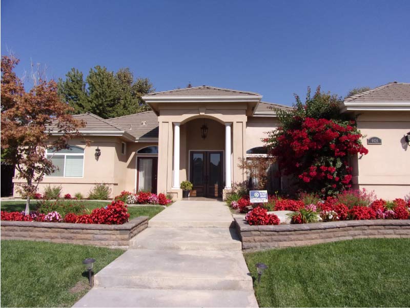 17 Creative Ways to Finance your Home Remodel: Front exterior view of a single-story home with a clean entryway, updated landscaping, and stone retaining wall, representing the successful completion of exterior house upgrades