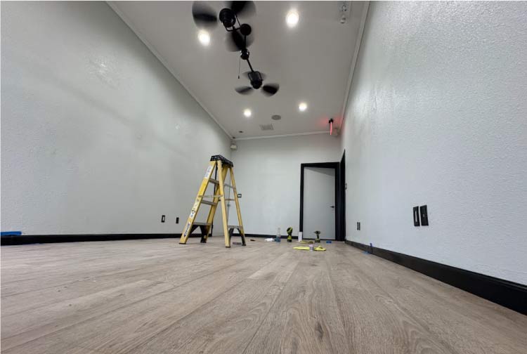 Wide interior shot of a remodeled room with new laminate flooring, fresh paint, modern ceiling fans, and recessed lighting, illustrating the quality of a whole-home renovation or ADU interior finish.