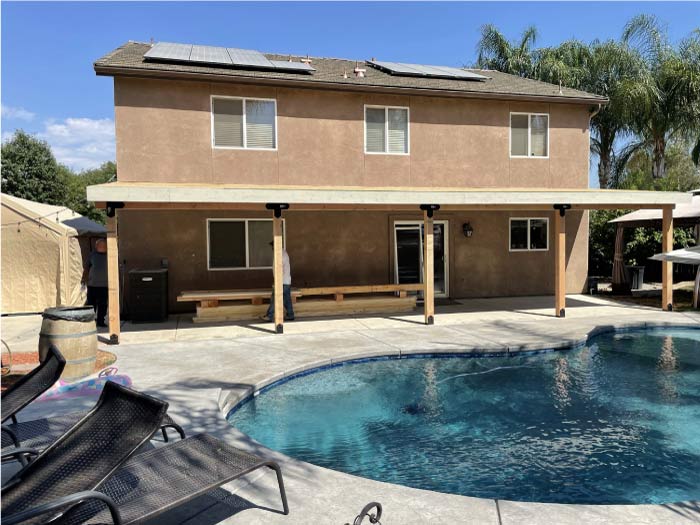 Finished view of a backyard shade structure (pergola/patio cover) with solar panels installed on top, demonstrating combined construction and energy-efficiency expertise.